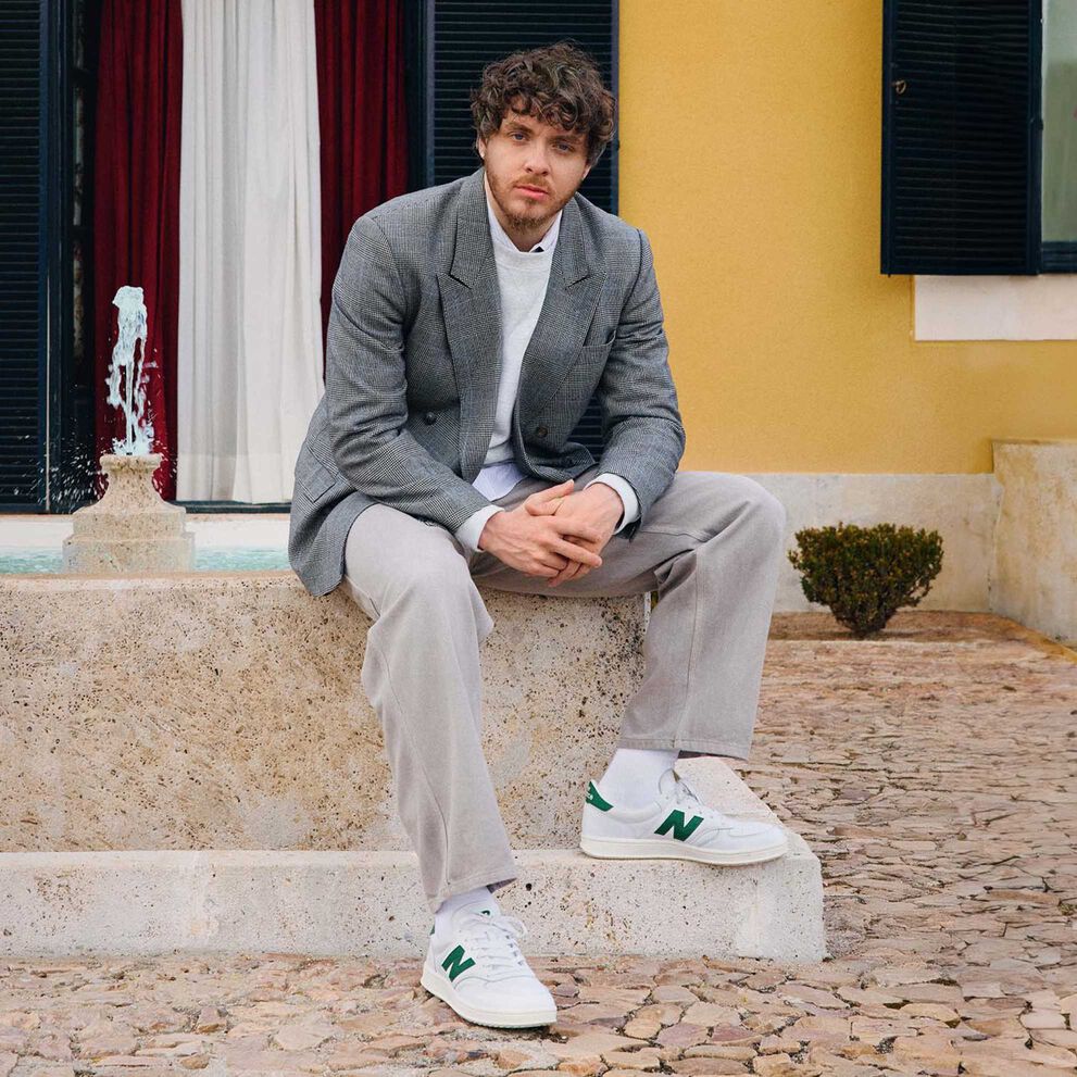 Jack Harlow assis à l’extérieur sur le rebord d’une fontaine.