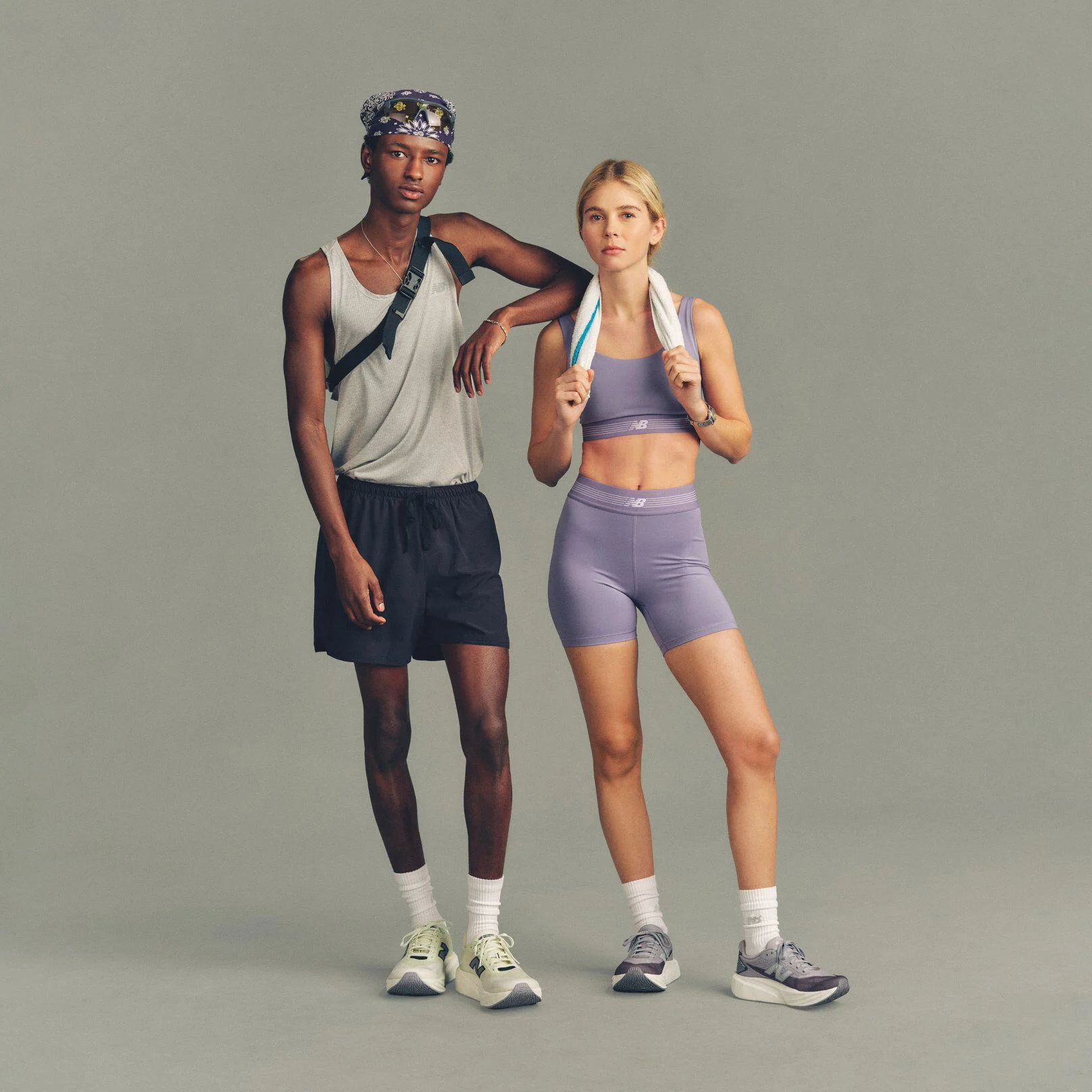 Two people stand side by side against a plain light gray studio background, wearing athletic apparel.