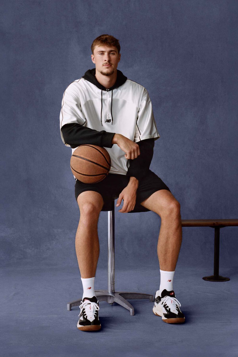 Cooper Flagg assis sur un banc, tenant un ballon de basket sur fond de studio bleu marine.
