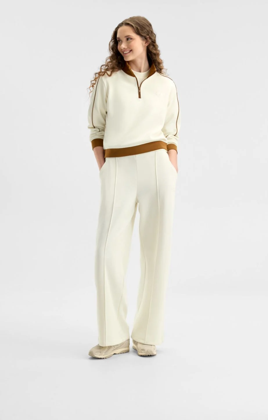 A woman wearing cream and brown New Balance gear on a white background.