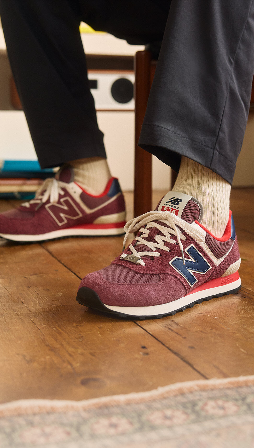 Knee down shot of a person wearing maroon 574 shoes.