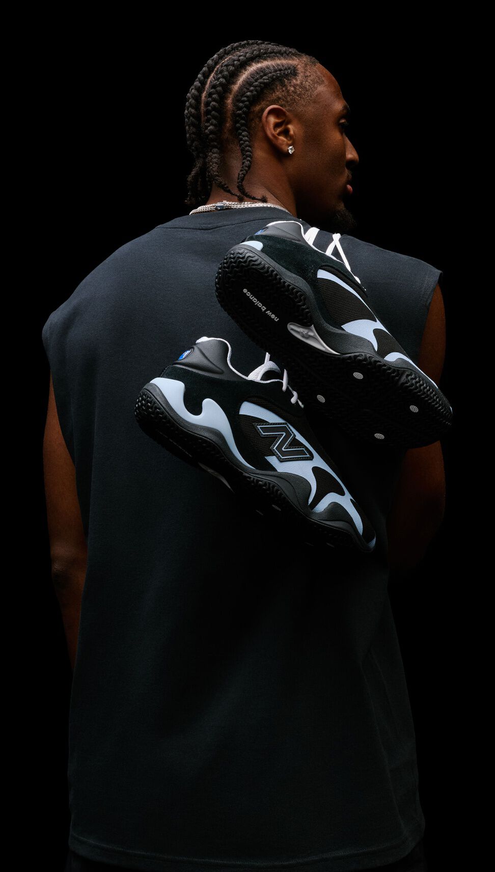 Studio portrait from behind featuring black-and-light-blue athletic sneakers suspended across a person's back against a black background.