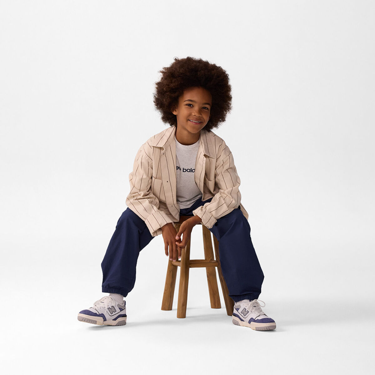 Young kid sitting on a stool wearing blue pants. 