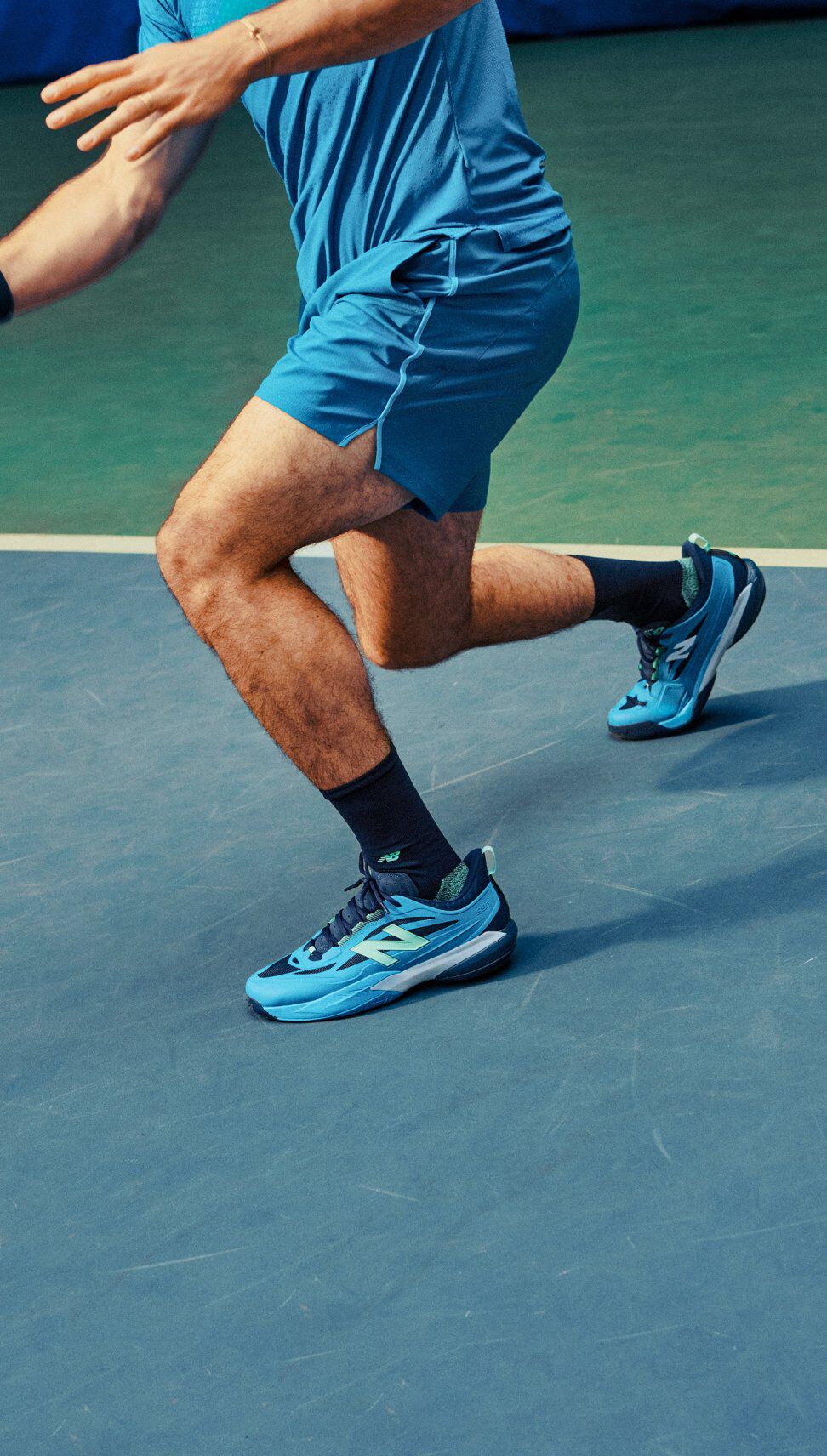 Un joueur de tennis se jette sur un court int&eacute;rieur portant des chaussures New Balance bleu vif pendant le jeu actif.