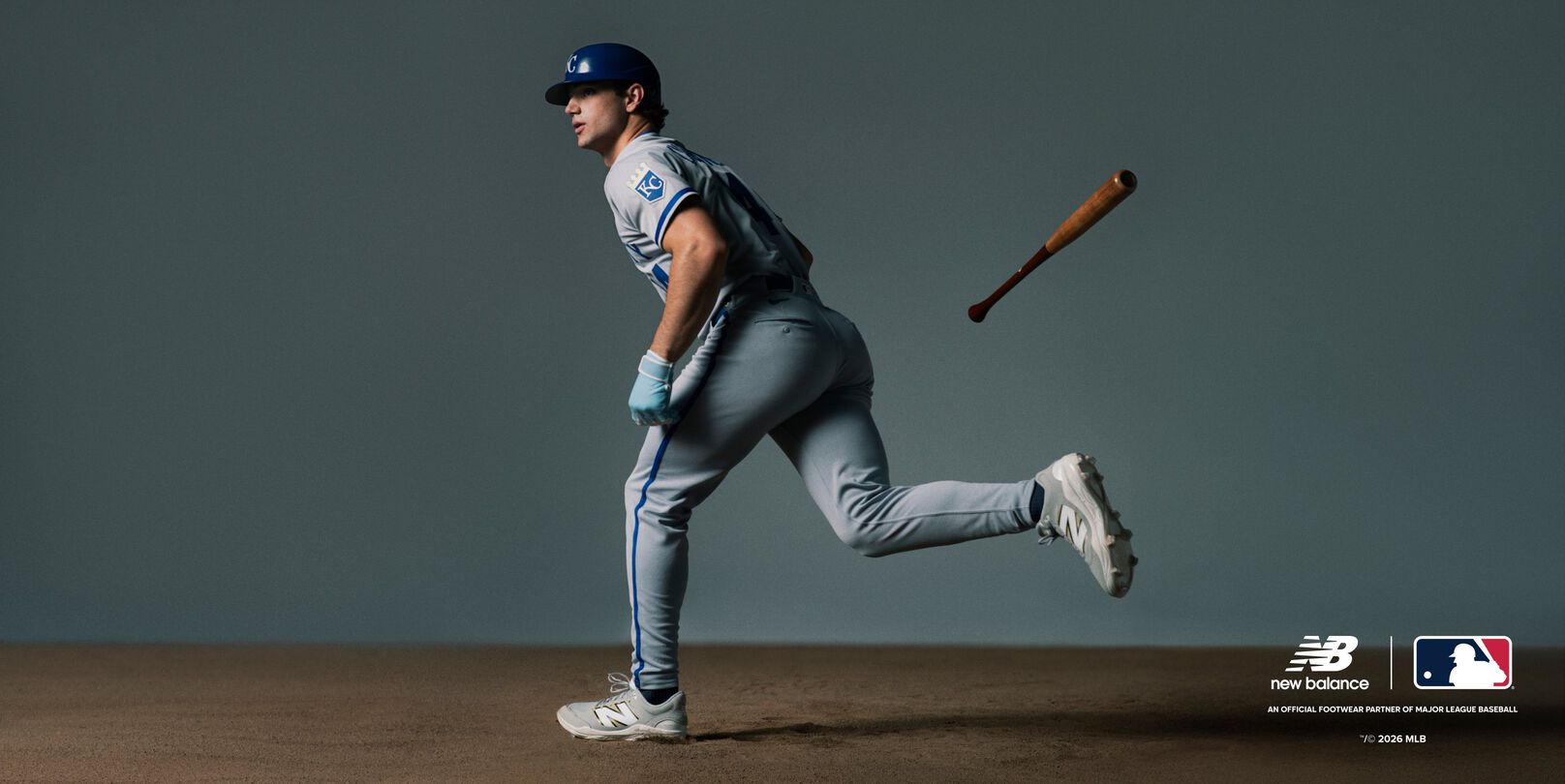 A baseball player wearing a light blue uniform with white and blue accents is running forward after swinging a bat, which is seen mid-air behind the player.