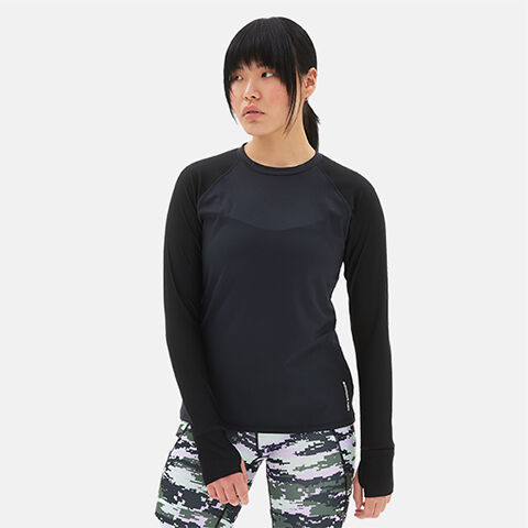 Woman standing in grey studio backdrop wearing black long sleeve shirt and printed leggings. 