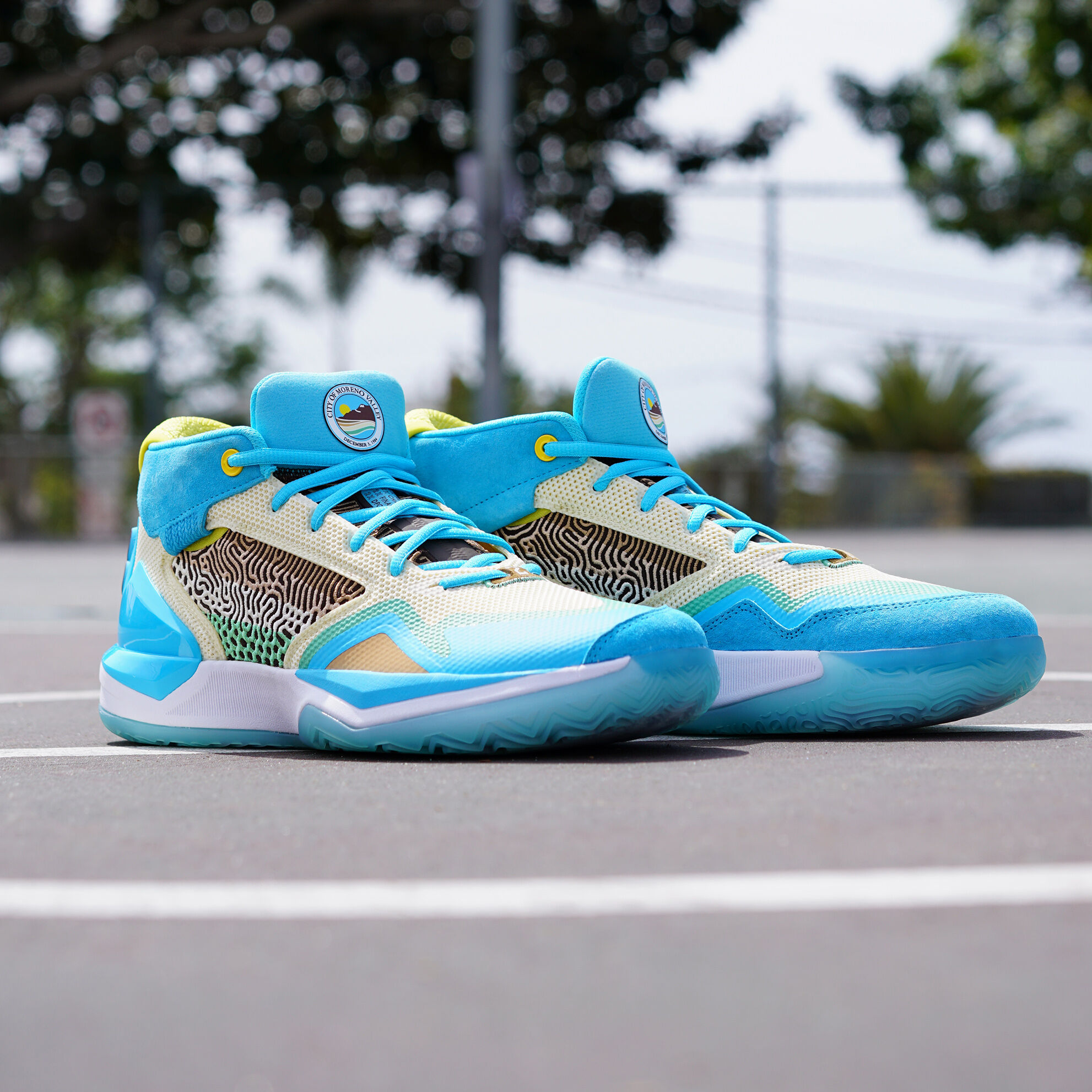 Side profile of a pair of light blue KAWHI Moreno Valley inspired basketball shoes sitting on the pavement of an outdoor basketball court