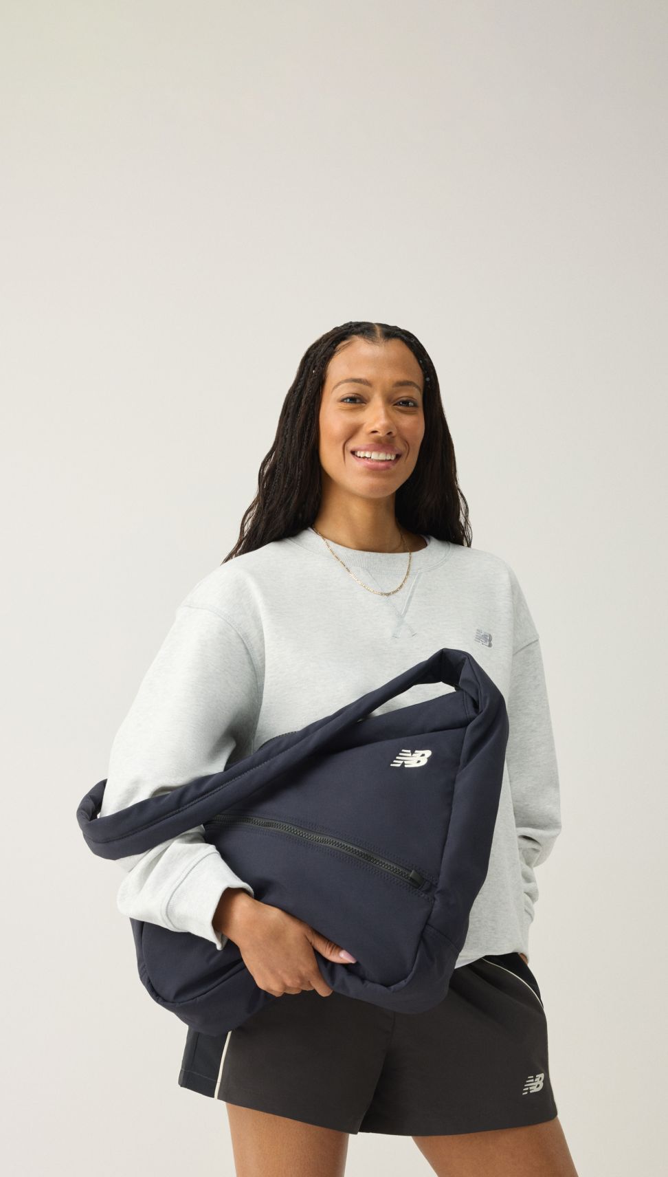 A woman looking at the viewer while holding a navy bookbag. 