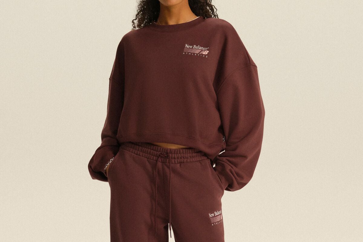 Personne portant un chandail molletonn&eacute; New Balance Athletics bordeaux et un pantalon de jogging assorti, dans un d&eacute;cor de studio &eacute;pur&eacute;.