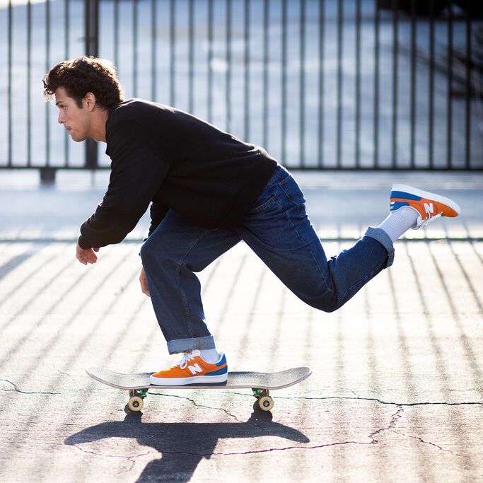 Vue de profil du patineur professionnel Ronnie Kessner, à mi-course sur sa planche à roulettes, portant des chaussures de skate orange NB Numeric 272