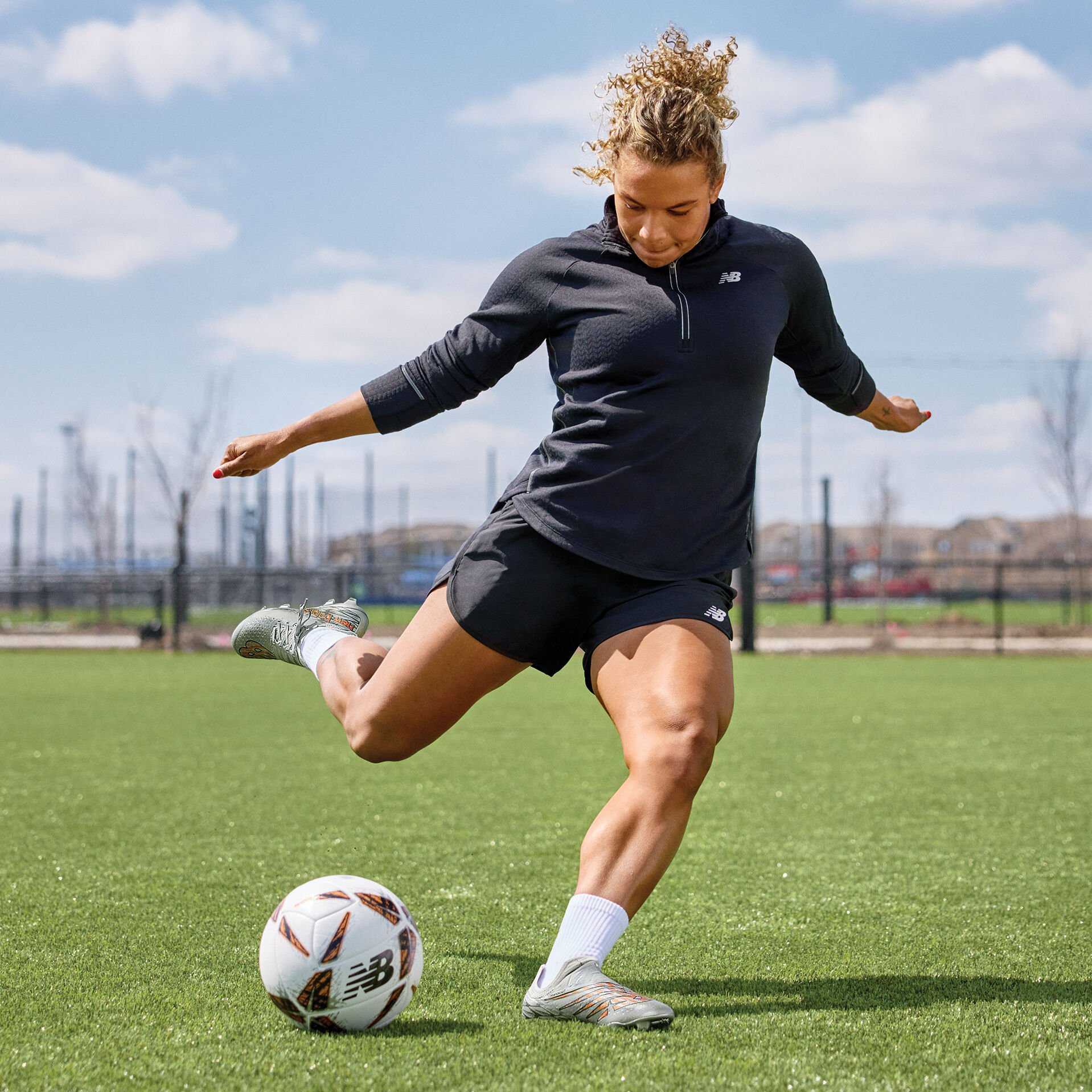 Young lady kicking a soccer ball on the pitch in a black uniform.    