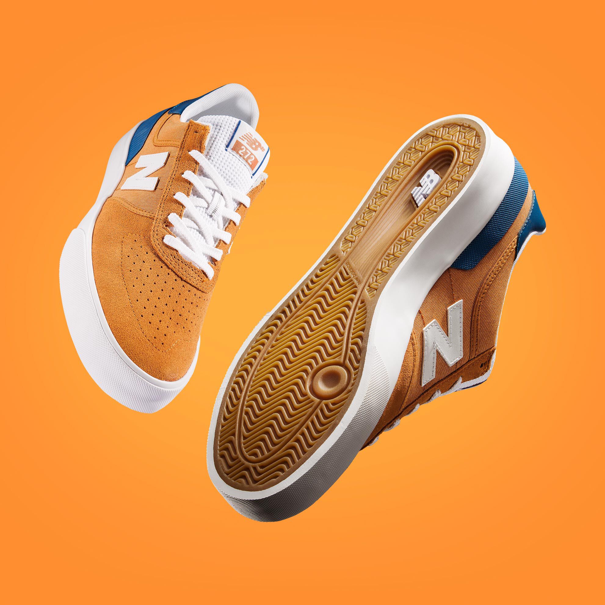 Une paire de chaussures de skate NB Numeric 272 orange et bleu flottant sur un fond orange
