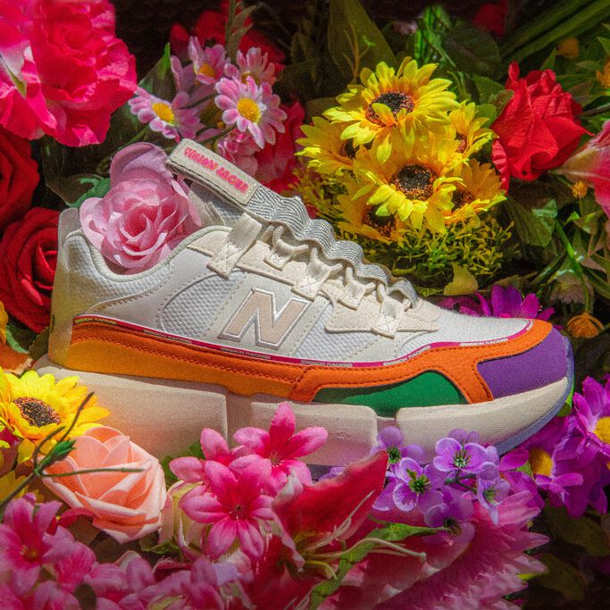 Vue en plongée d'une chaussure Vision Racers blanche rehaussée d'accents de multiples couleurs sur un lit de fleurs.