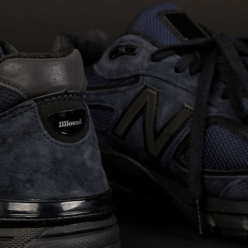 Une paire d’espadrilles NB 990v4 bleu marine sur un fond de studio gris foncé.