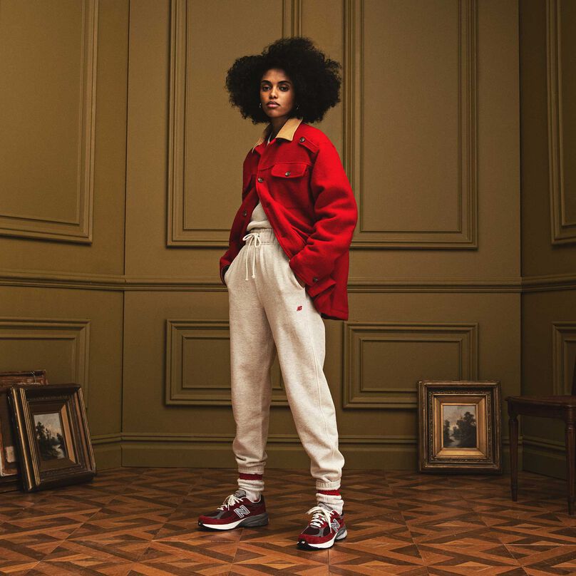 Femme debout dans un bel environnement intérieur et portant des vêtements chaussures MADE in USA de New Balance et des 990v3 rouges.