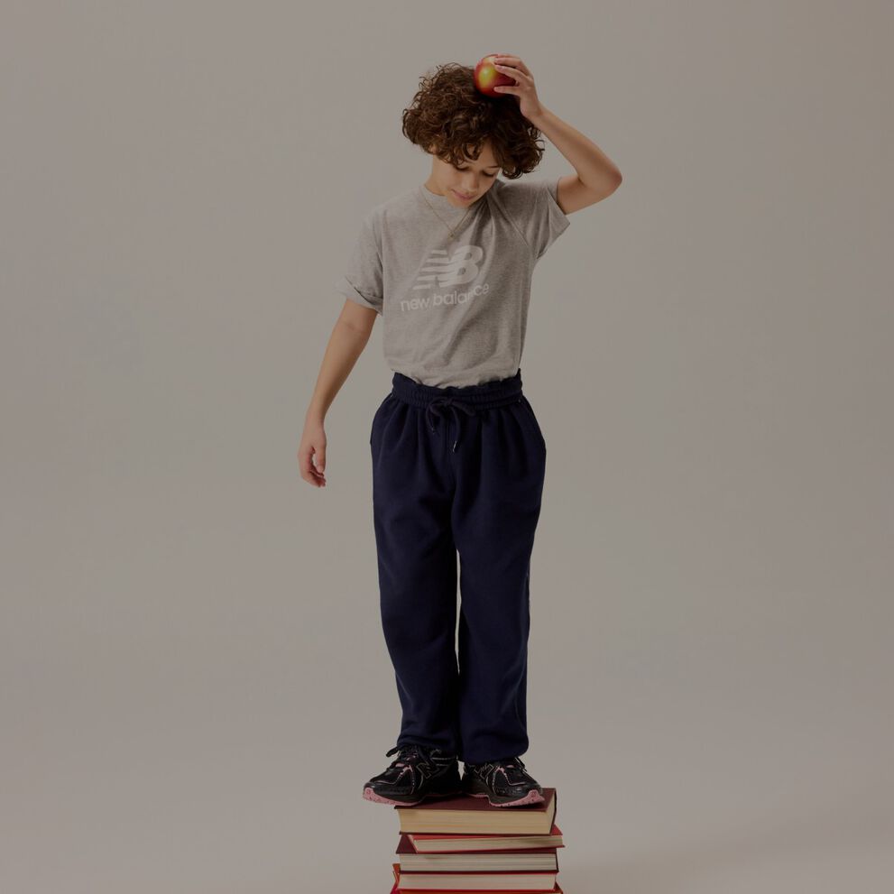 Kid standing on books holding an apple over his head.