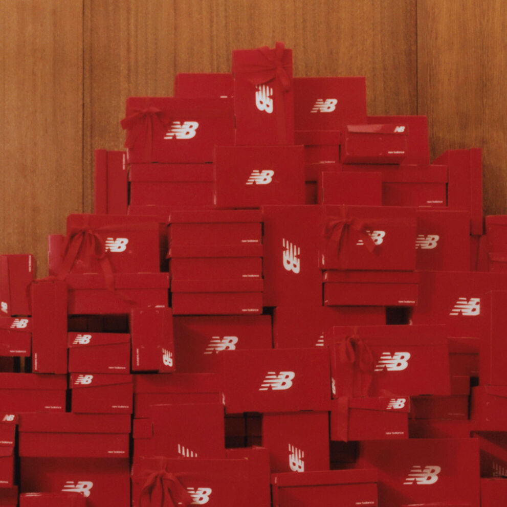 Une grande pile de boîtes à chaussures New Balance rouges avec des arcs rouges attachés en hauteur contre un mur de panneaux de bois
