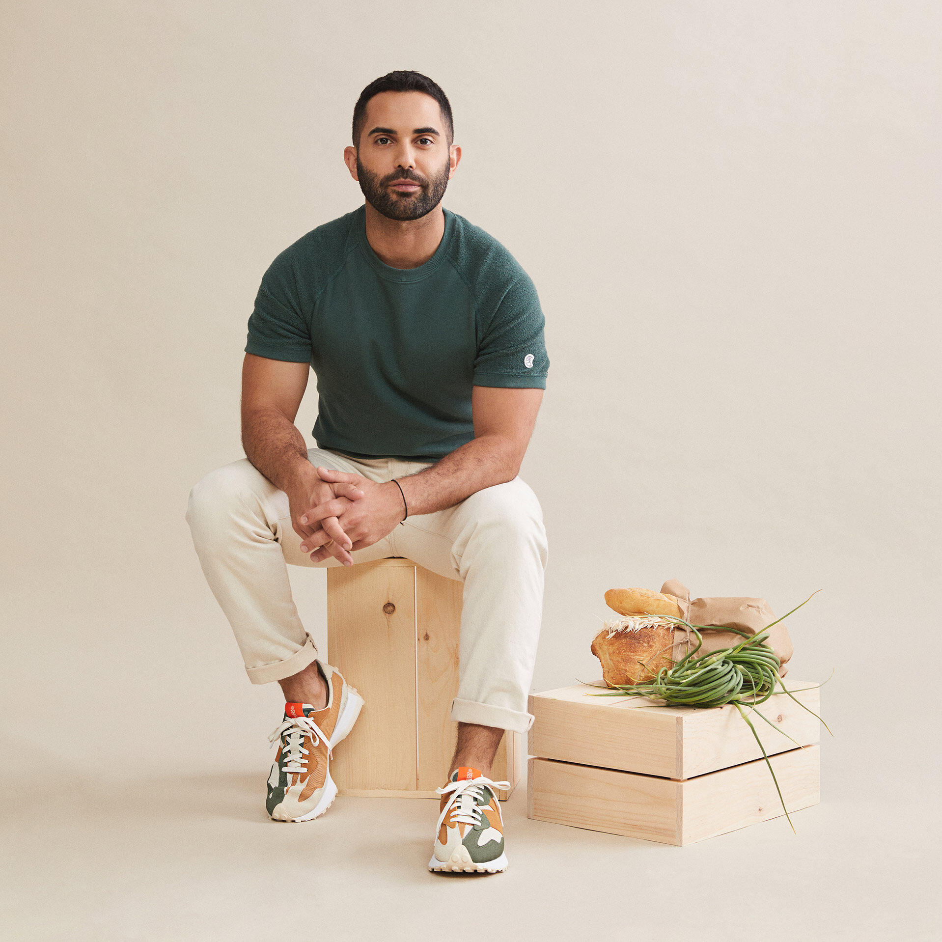 Assise dans un studio sur une boîte en bois à côté de pains et d'une gerbe de blé, le chef Andy Baraghani porte des chaussures 327 de couleurs olive, beige et brun roux