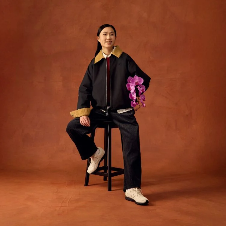 Woman smiling and sitting on a stool holding flowers.