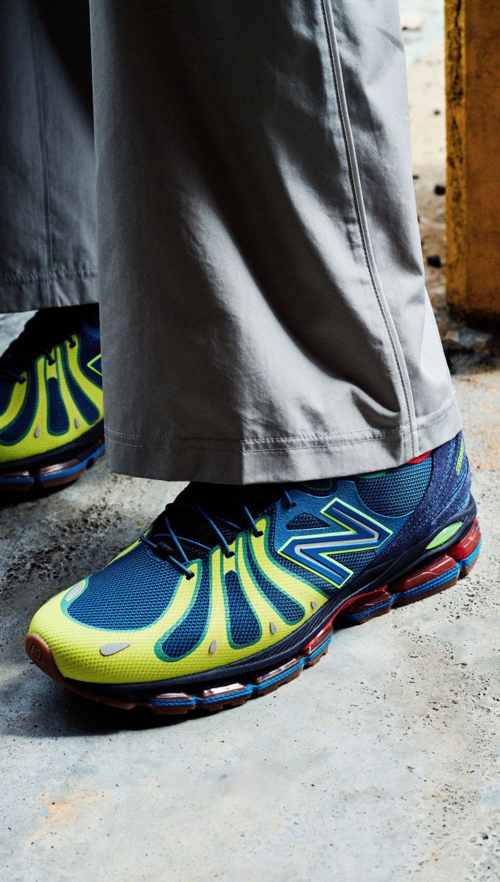 Close-up of someone wearing blue and green New Balance sneakers on a concrete background. 