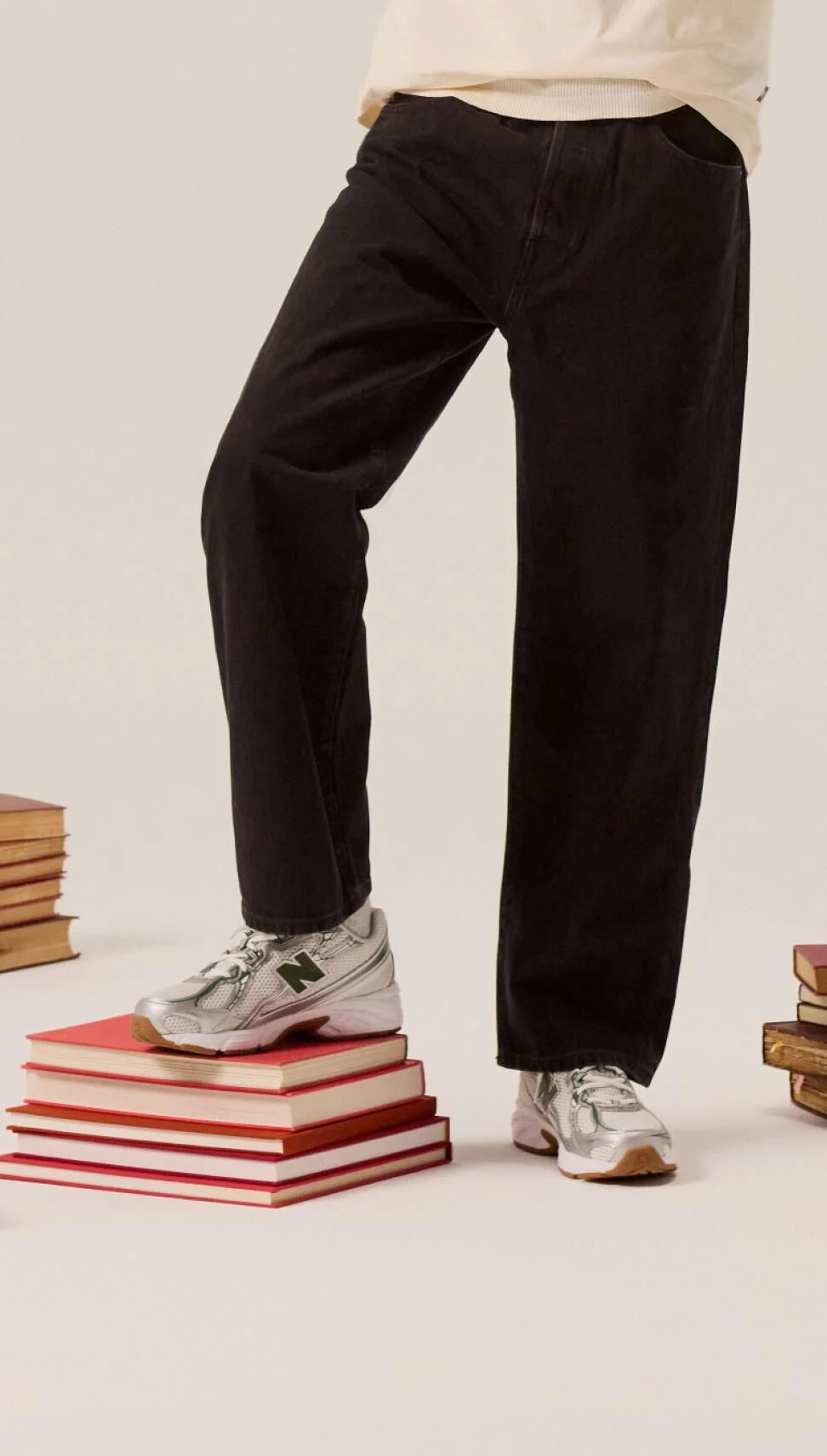Un étudiant en pantalon noir s'appuie sur une pile de livres. 