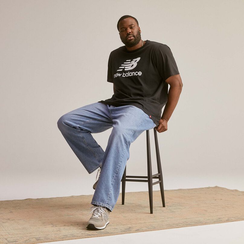 Un homme assis sur un tabouret portant un t-shirt Essentials à logo Stacked.