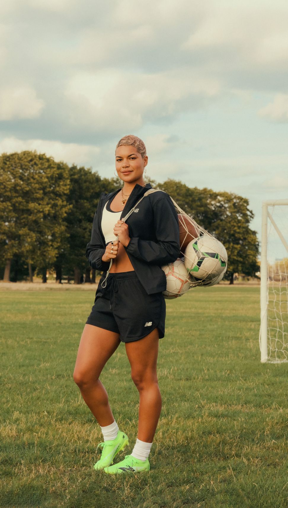 Female soccer player wearing black shorts holding a bag of soccer balls.	