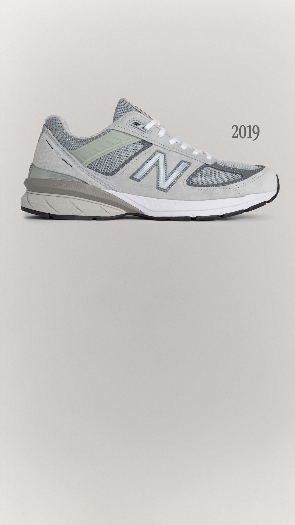 A grey 990v5 sneaker sitting on a grey background.