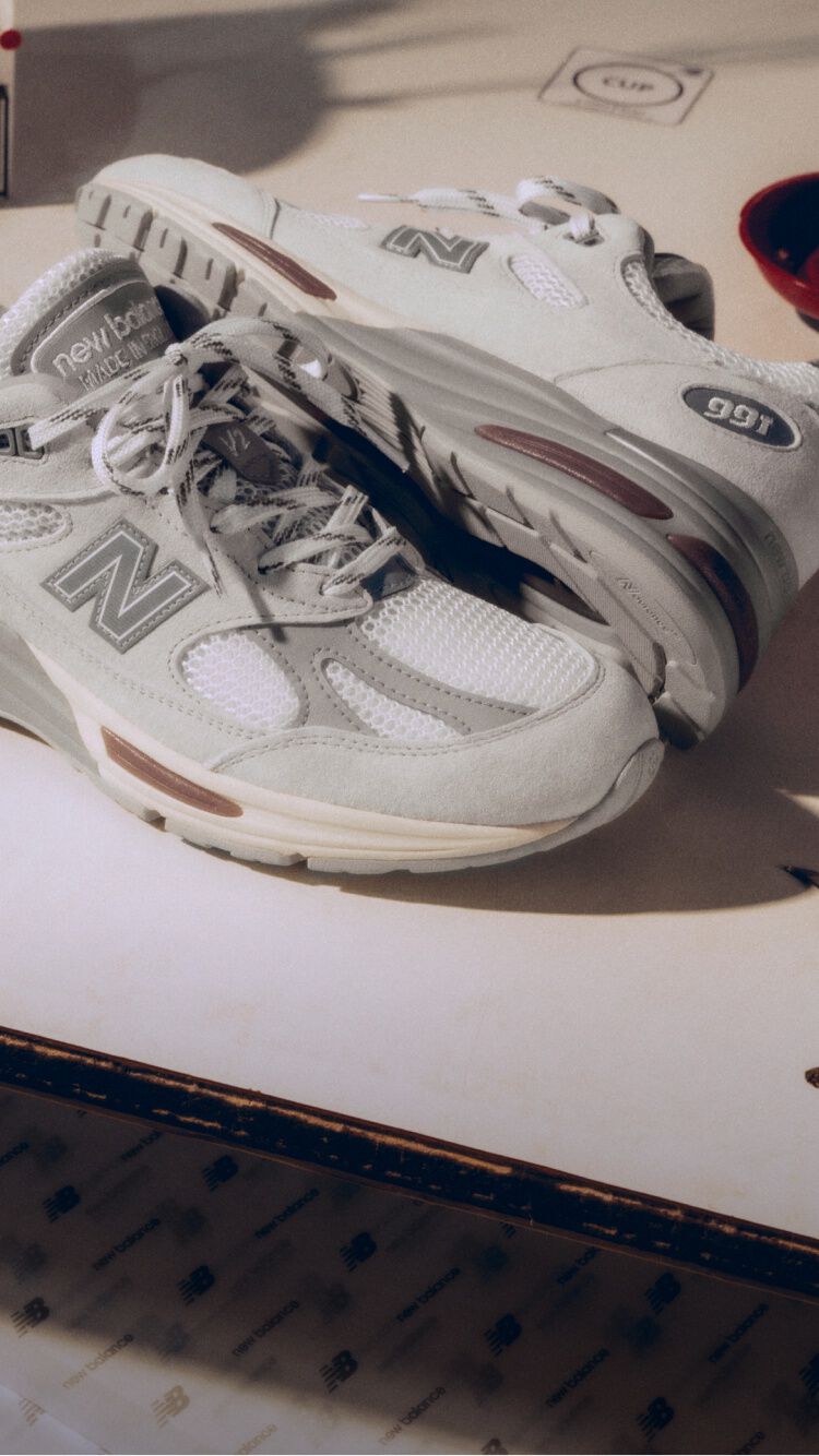 A pair of New Balance Made in UK sneakers on a white workbench surrounded by shoemaking tools and other textile equipment.