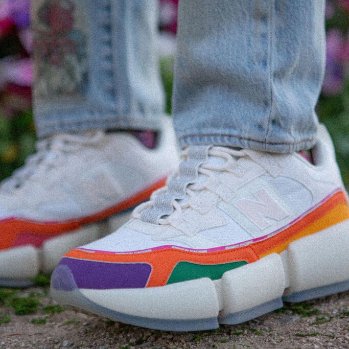 Vue à partir des genoux d'une personne vêtue d'une paire de chaussures Vision Racers blanches rehaussées d'accents de multiples couleurs.