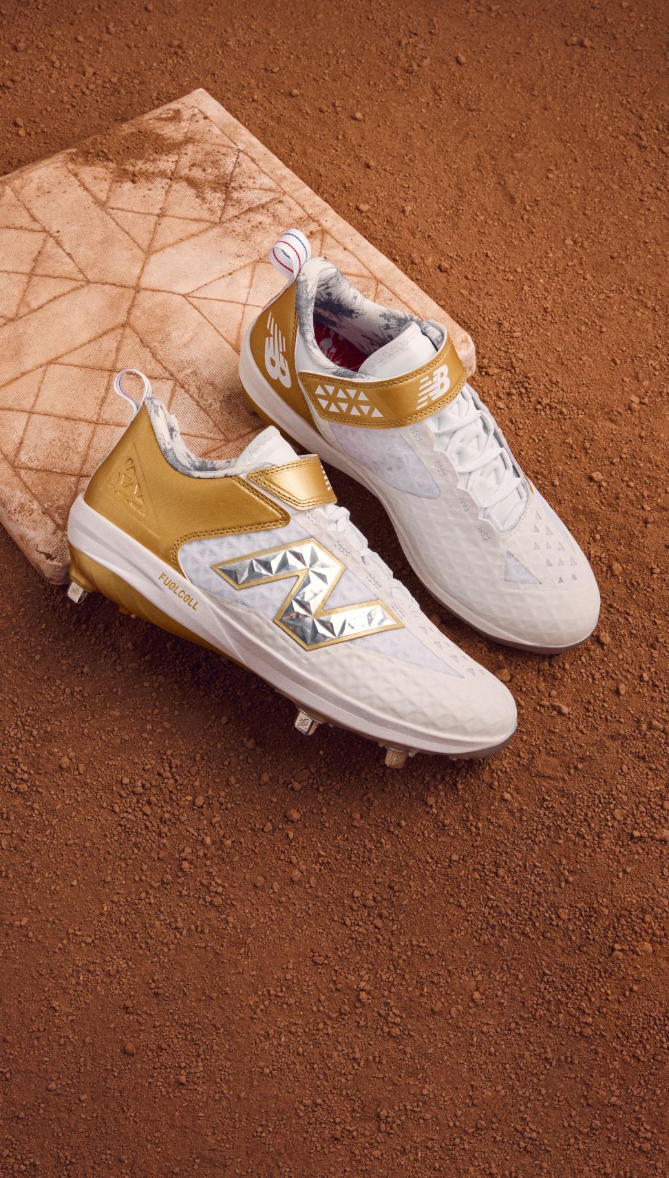 Pair of gold and white cleats sitting on a base surrounded by dirt. 