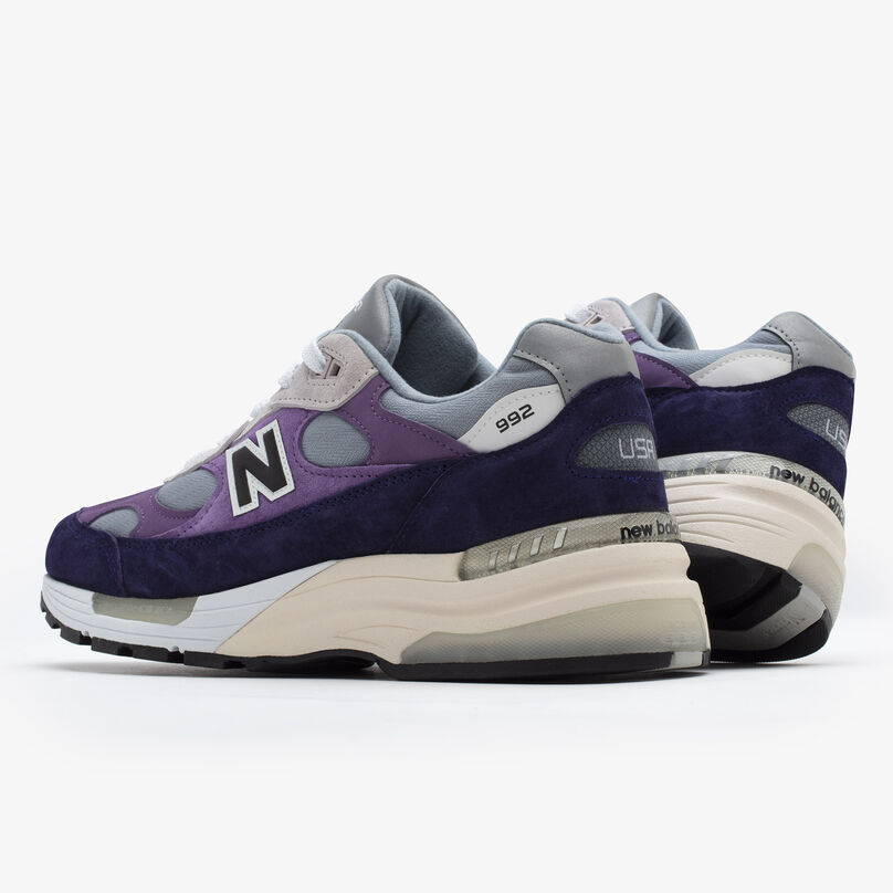Pair of purple 992 sneakers on a grey studio environment pointing away from camera to show back details.
