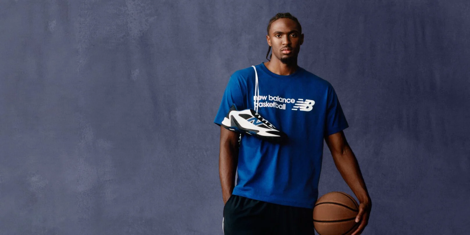 A person wearing a blue New Balance Basketball T‑shirt poses against a plain backdrop.