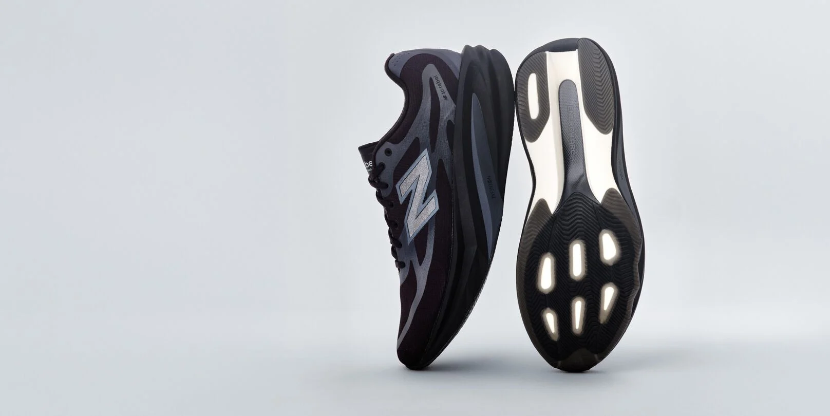 A pair of black New Balance sneakers sitting on a gray studio backdrop. 