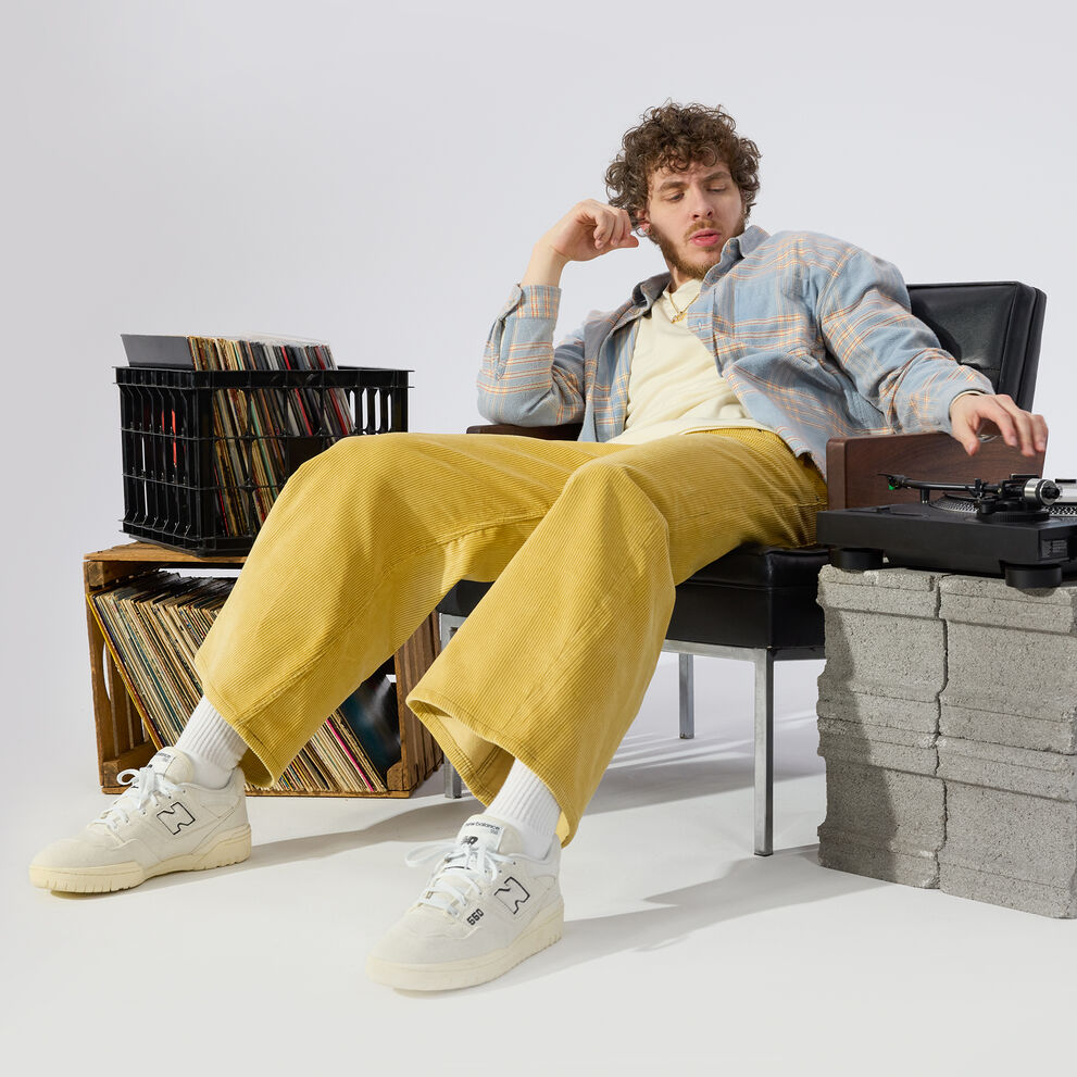 Jack Harlow assis sur une chaise, dans un pantalon jaune en train de mixer.