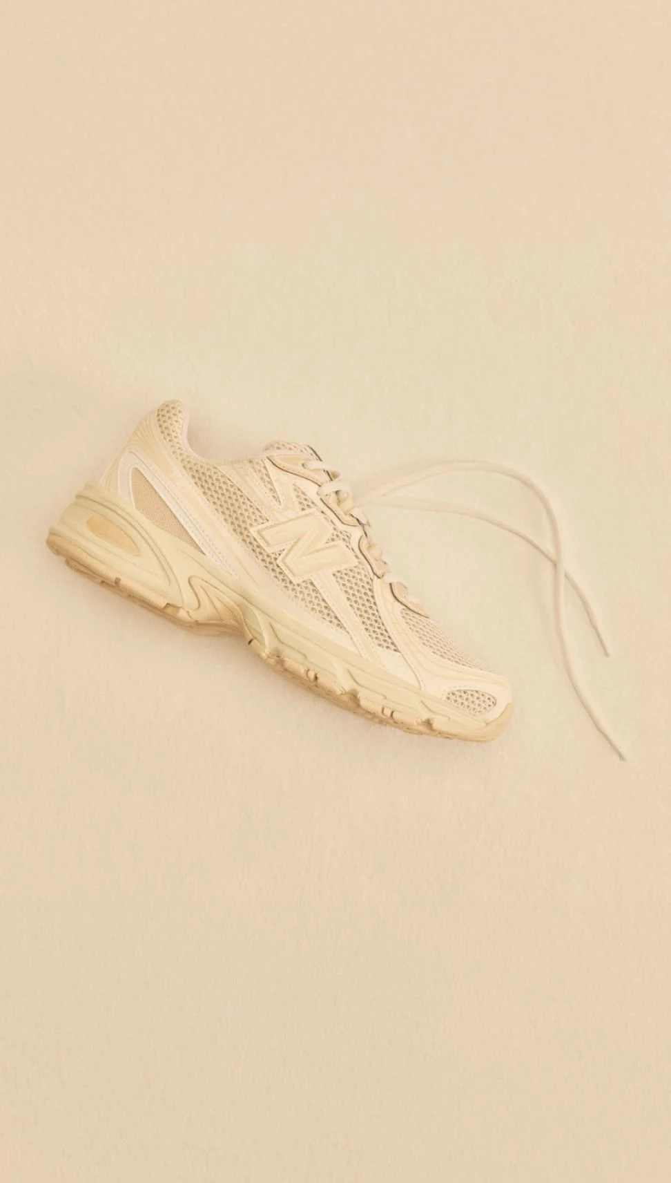 A tan shoe laying on a tan studio backdrop.