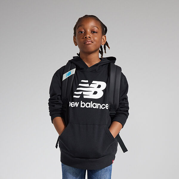 Image à partir de la taille d’un jeune garçon debout avec assurance, portant un chandail à capuche NB Essentials noir, un pantalon jean et un sac à dos NB noir 