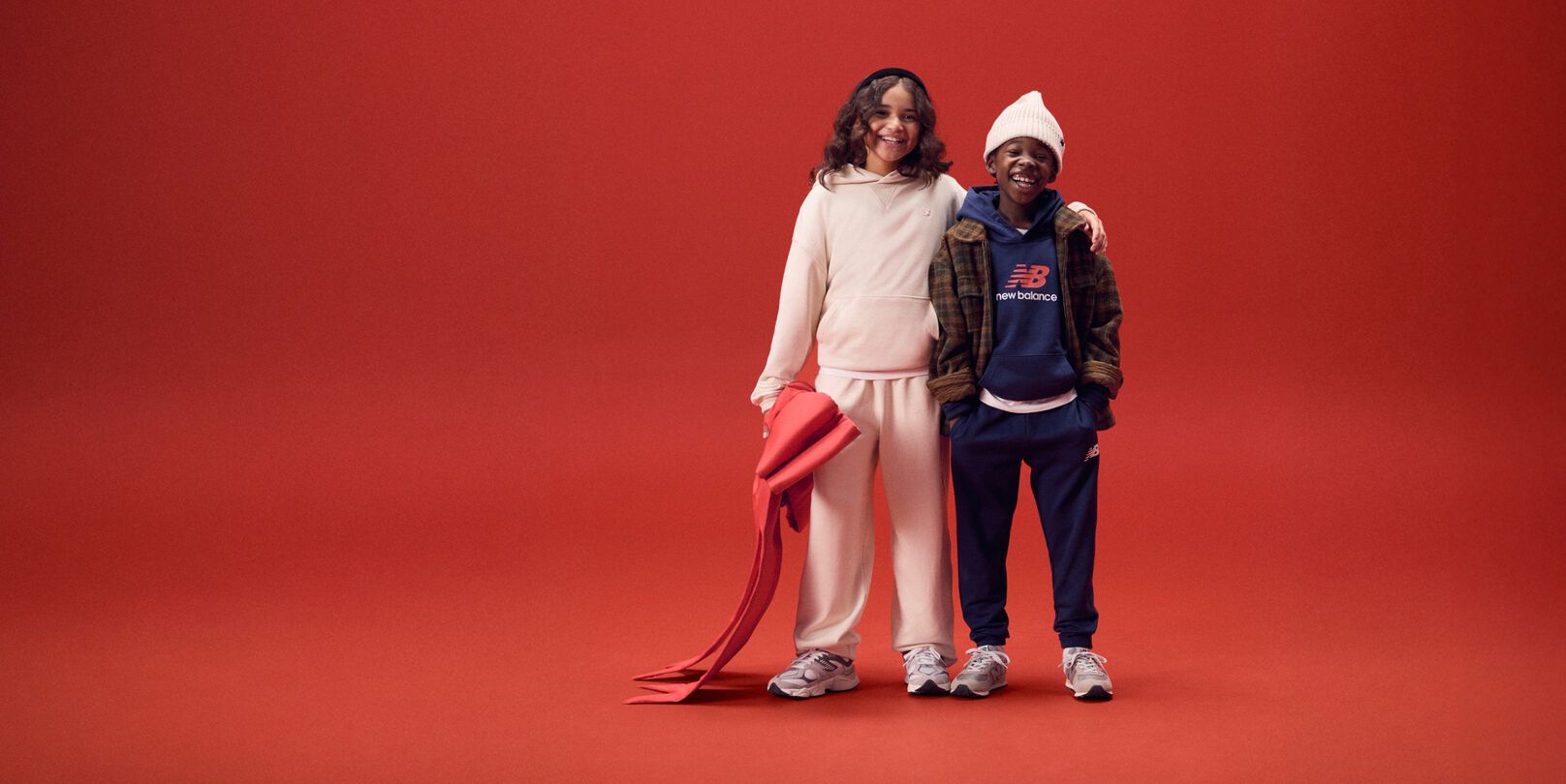 Deux jeunes enfants souriant, bras dessus sur un fond rouge.