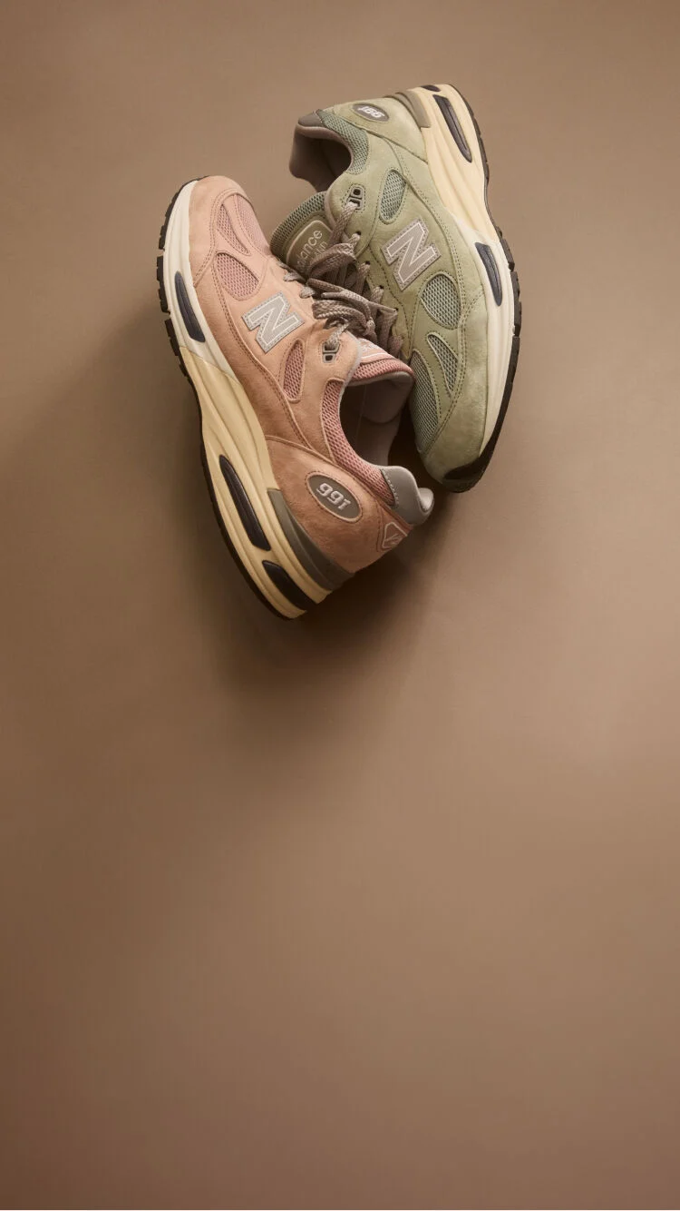 Top down view of two New Balance Made in UK sneakers resting against one another in a beige studio environment. 