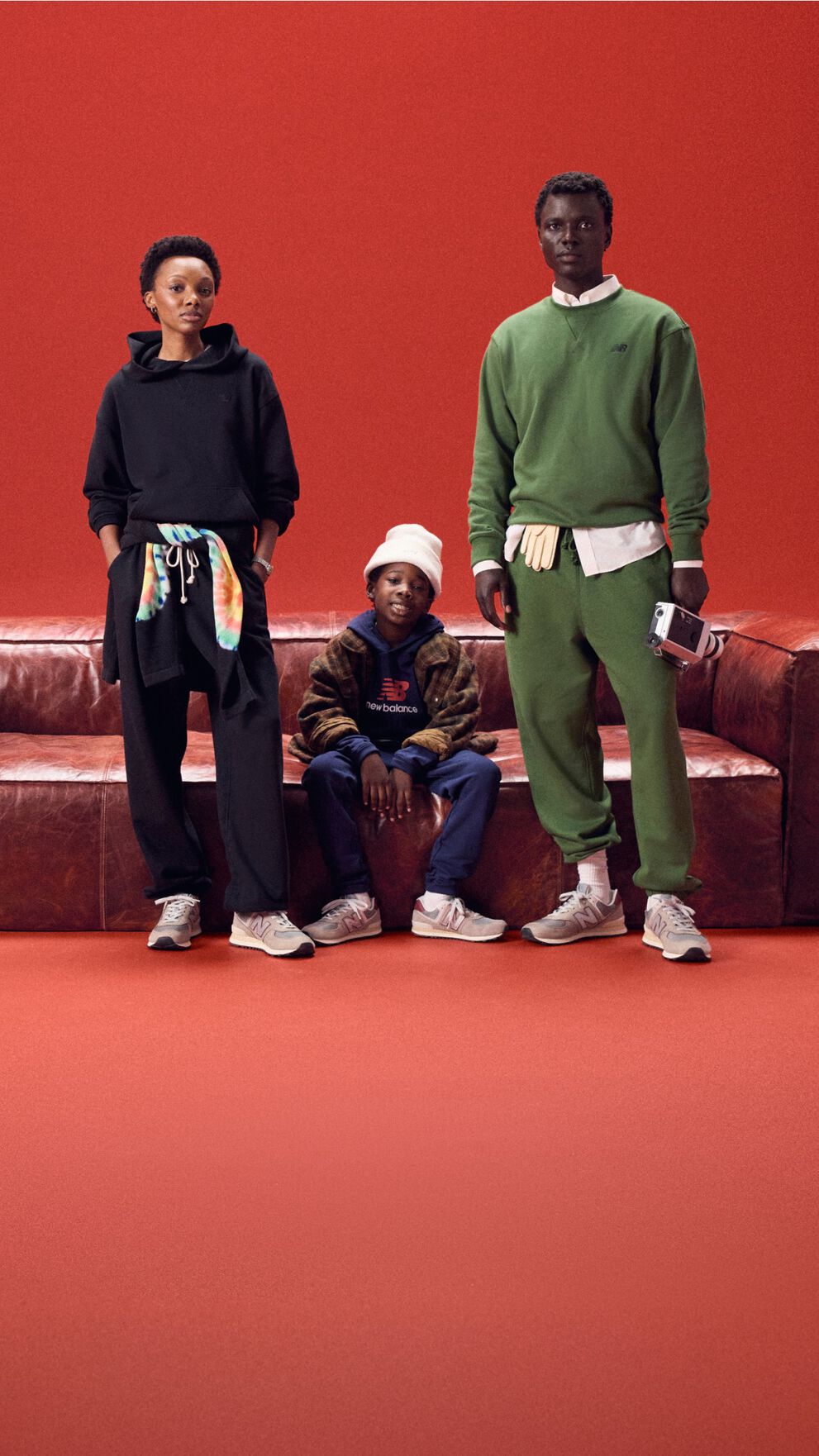 Famille de trois assise sur un canapé en cuir rouge sur fond rouge.