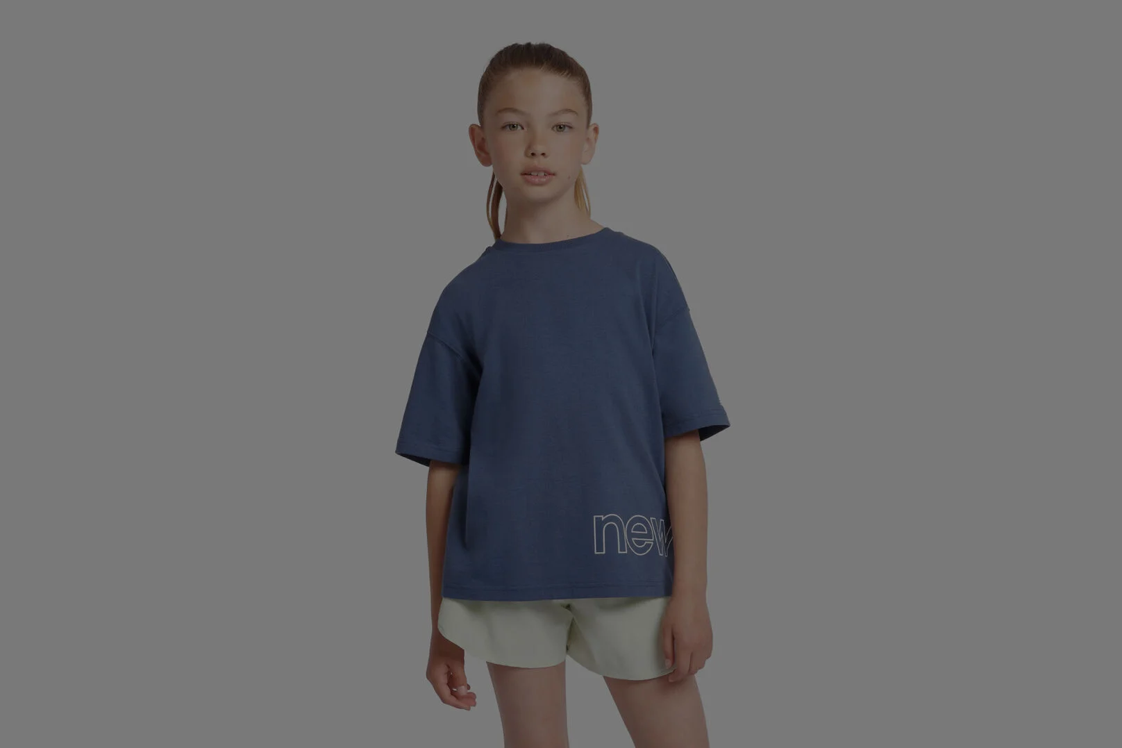 Enfant portant un maillot New Balance bleu sur fond gris.