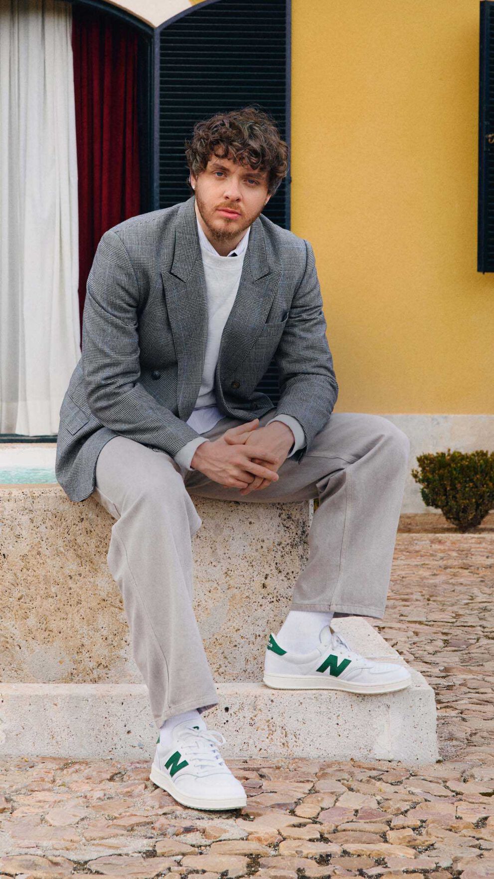 Jack Harlow sitting outside on a fountain. 