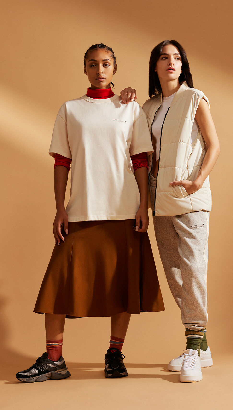 Two women wearing NB Uni-ssentials clothing, posing in front of a burnt orange studio backdrop 