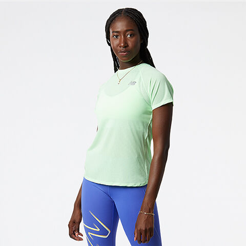 Woman standing in grey studio backdrop wearing green t-shirt and blue leggings. 