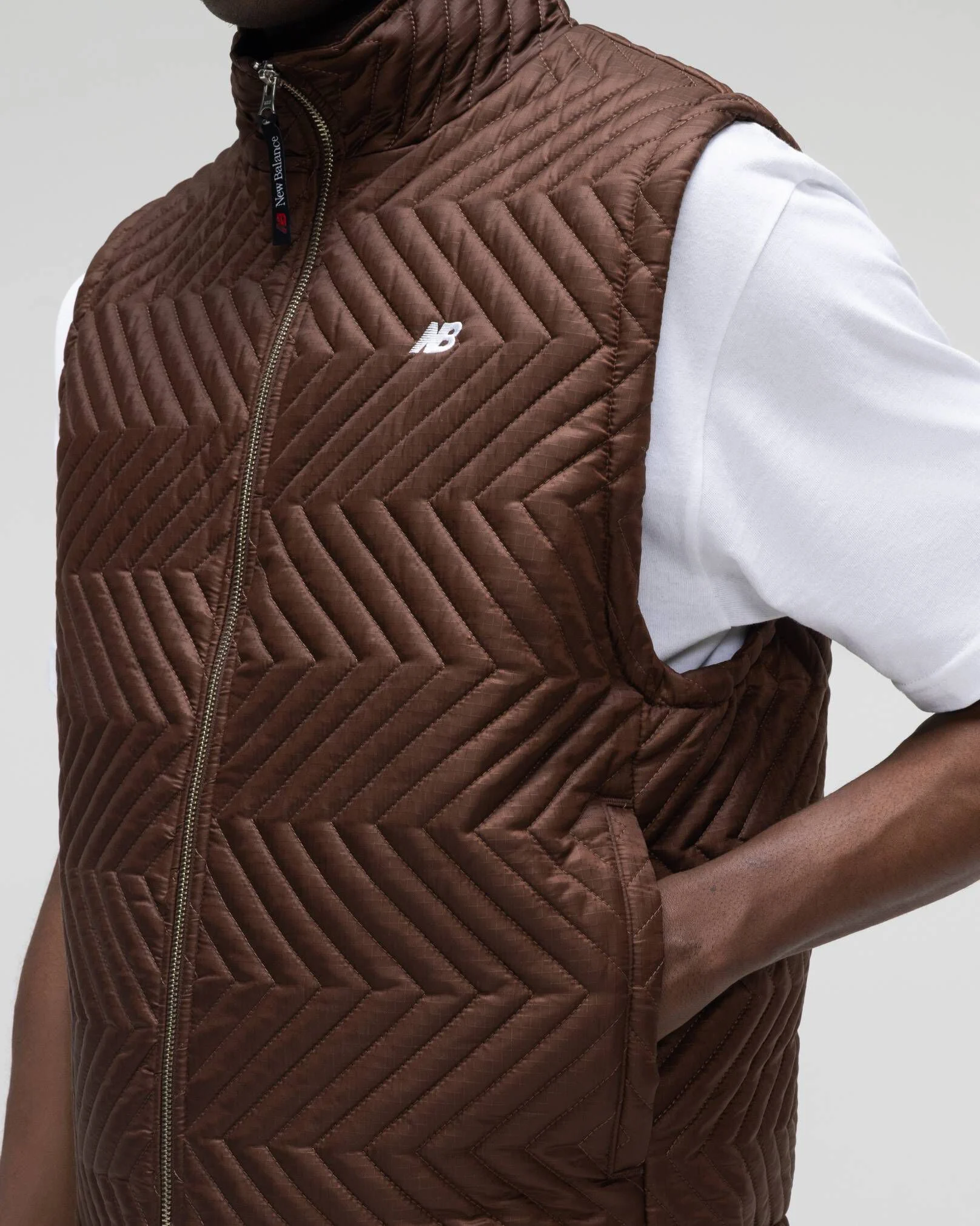 Une personne v&ecirc;tue d'un cardigan marron, debout devant un fond de studio gris