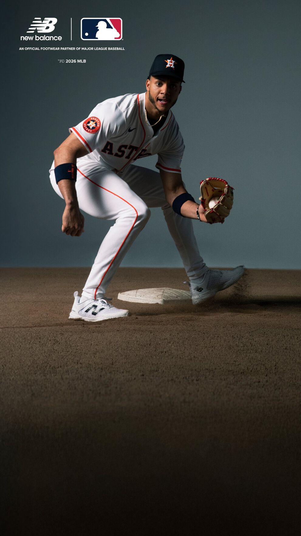 A baseball player wearing a white Houston Astros uniform with orange accents is in a ready fielding stance on a dirt infield.