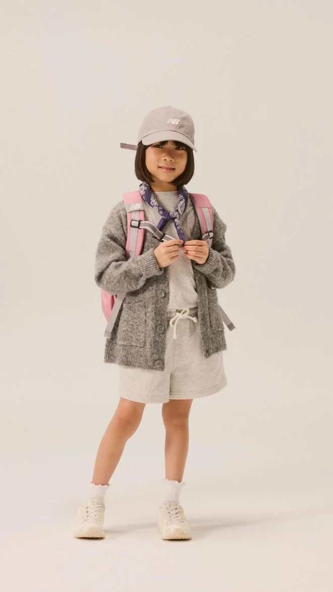 Young kid wearing a hat, jacket and pink backpack with white shoes. 