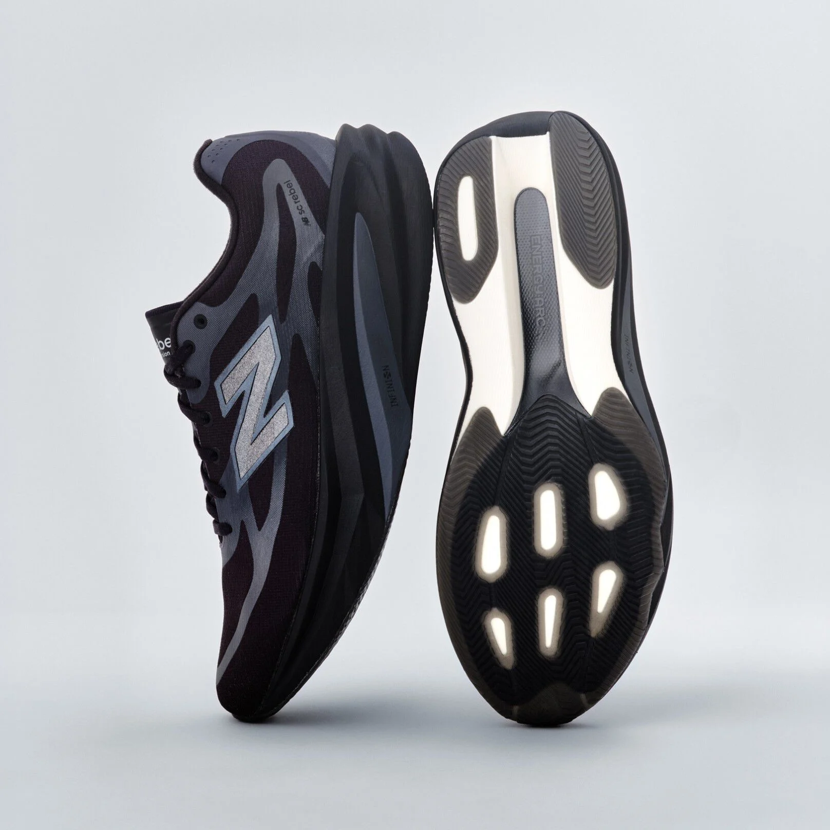 A pair of black New Balance sneakers sitting on a gray studio backdrop. 