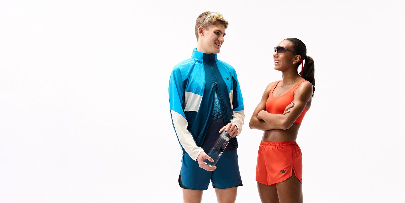 Deux personnes en tenues sportives color&eacute;es se font face sur un fond blanc uni, l&rsquo;une tenant une bouteille d&rsquo;eau, toutes deux portant des accessoires sportifs et apparaissant en plein milieu d&rsquo;une conversation.