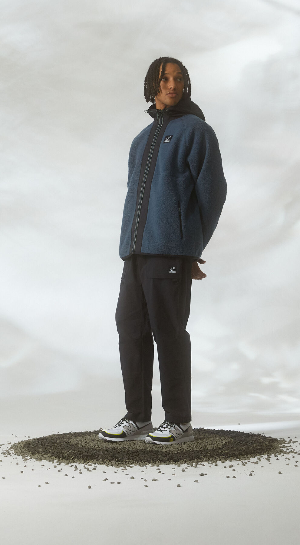 Man standing in gravel against cloudy studio environment wearing All Terrain gear and 574 shoes